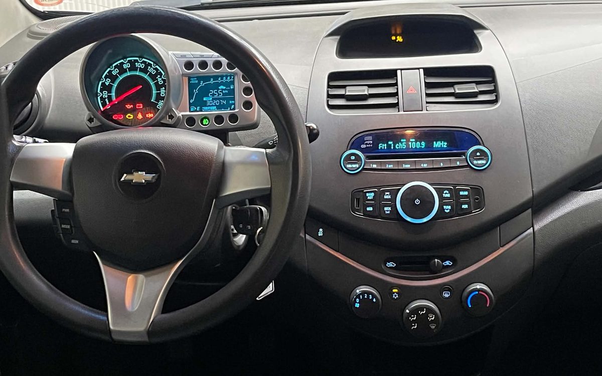 Instrumentbrættet i den sorte Chevrolet Spark med rat, radio og klimaanlæg