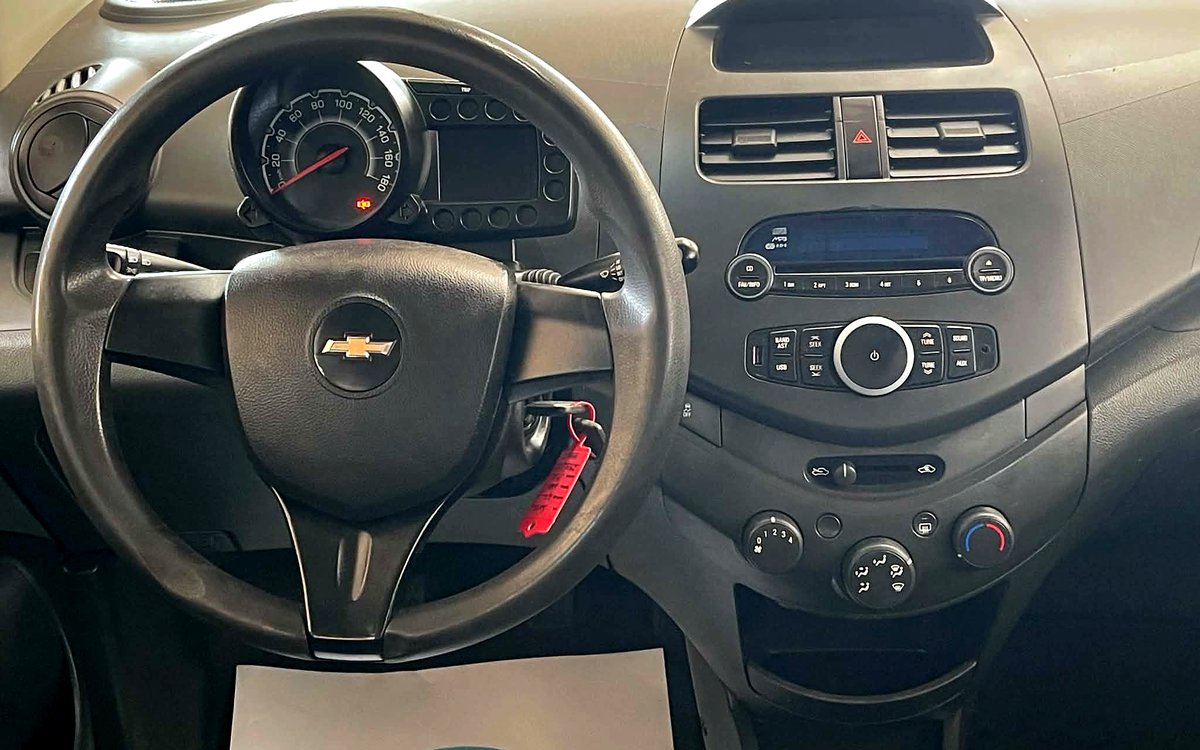 Instrumentbrættet i den hvide Chevrolet Spark med rat, radio og manuelt gear