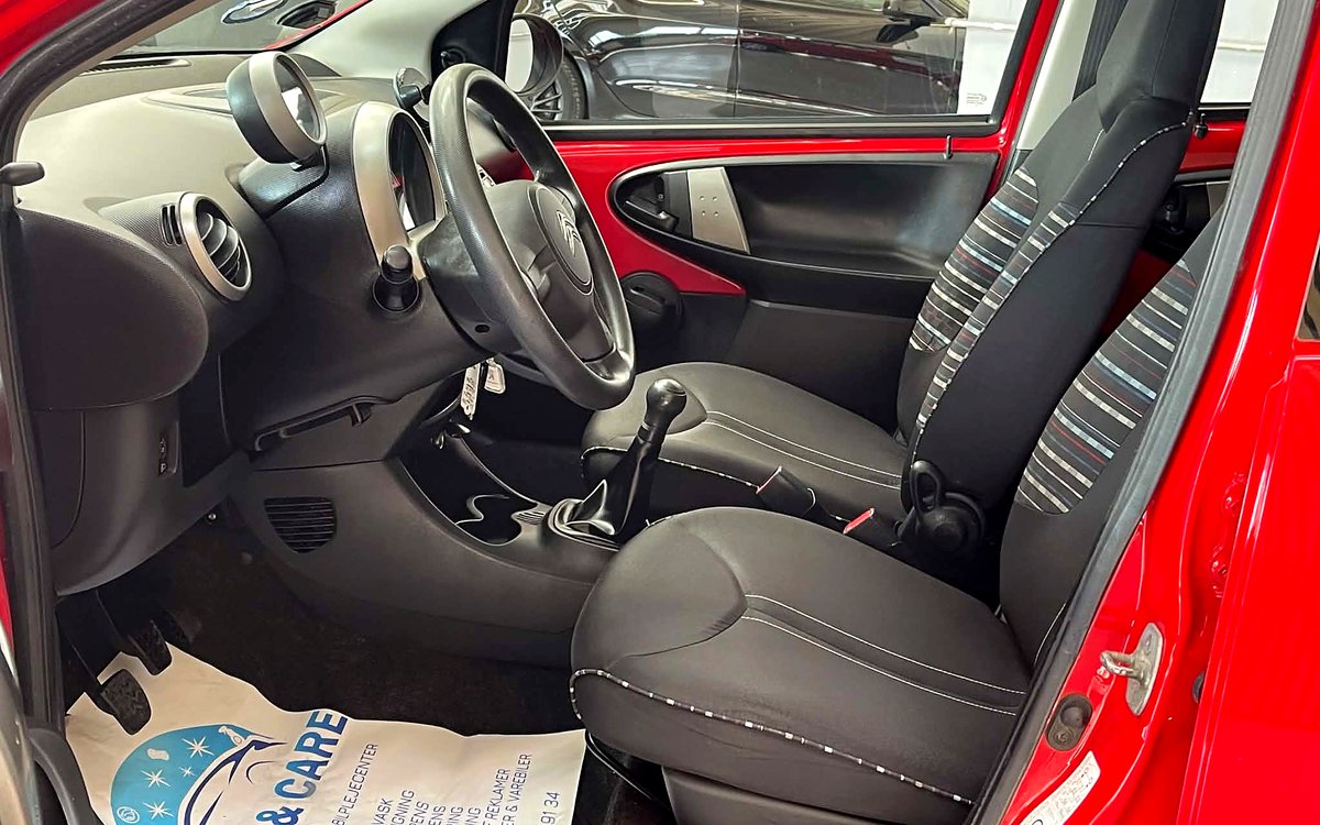Førerpladsen i den røde Citroën C1 med rat, manuelt gear og stofsæder