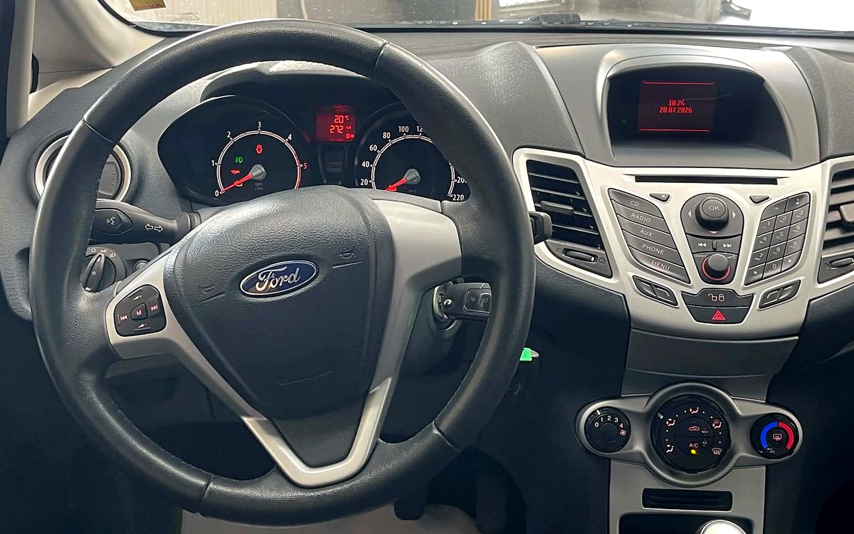 Instrumentbrættet i den grå Ford Fiesta med rat, radio, aircondition og manuelt gear