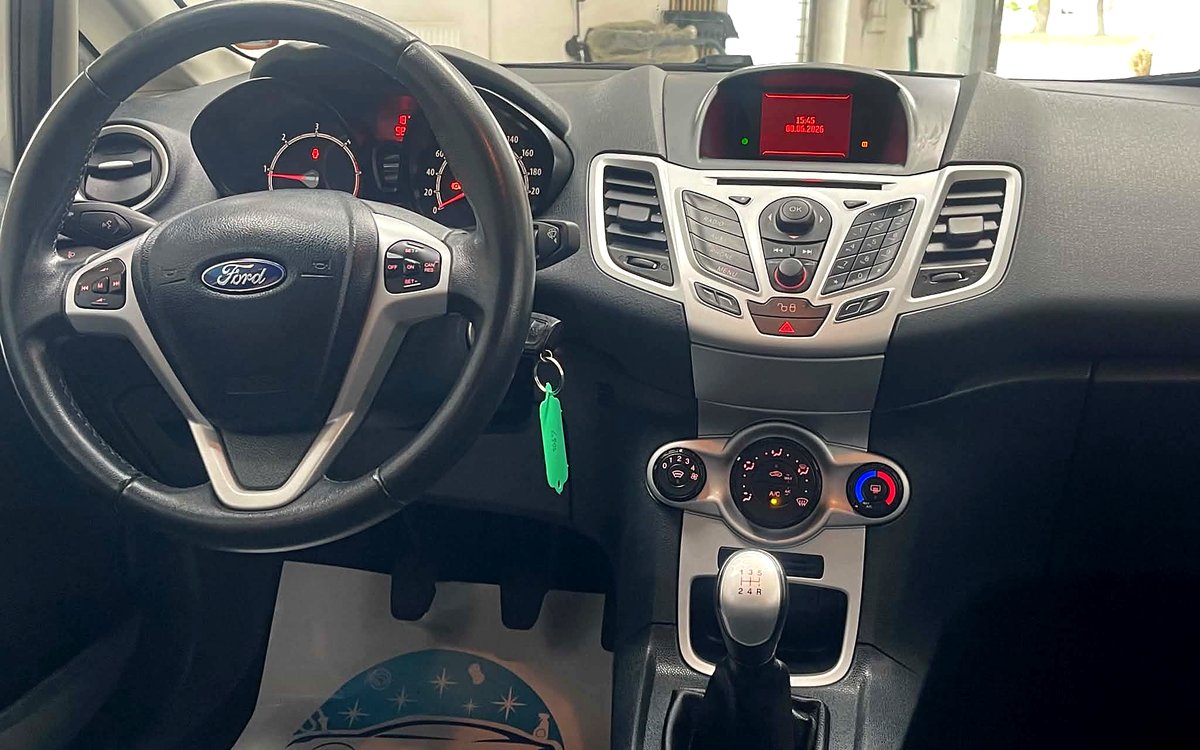 Instrumentbrættet i den hvide Ford Fiesta med radio, aircondition og manuelt gear