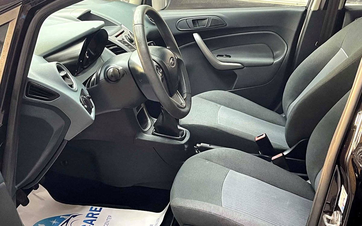 Førerpladsen i den sorte Ford Fiesta med rat, manuelt gear og stofsæder