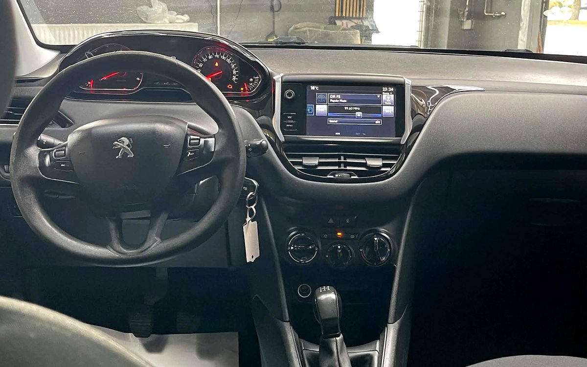 Instrumentbrættet i den beige Peugeot 208 med rat, touchskærm, klimaanlæg og manuelt gear