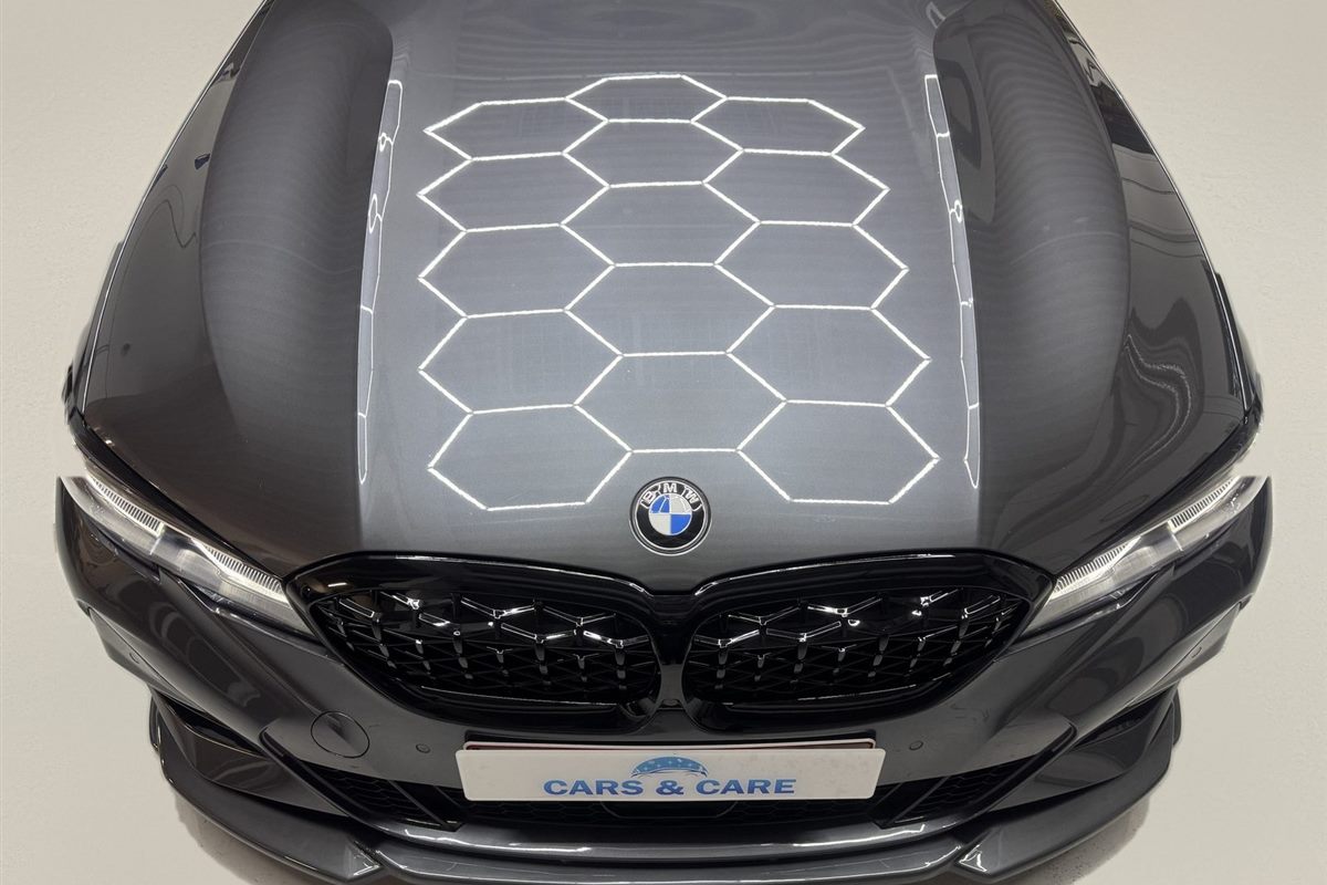Poleret mørkegrå motorhjelm på en BMW, hvor værkstedets sekskantede lys spejler sig skarpt i lakken