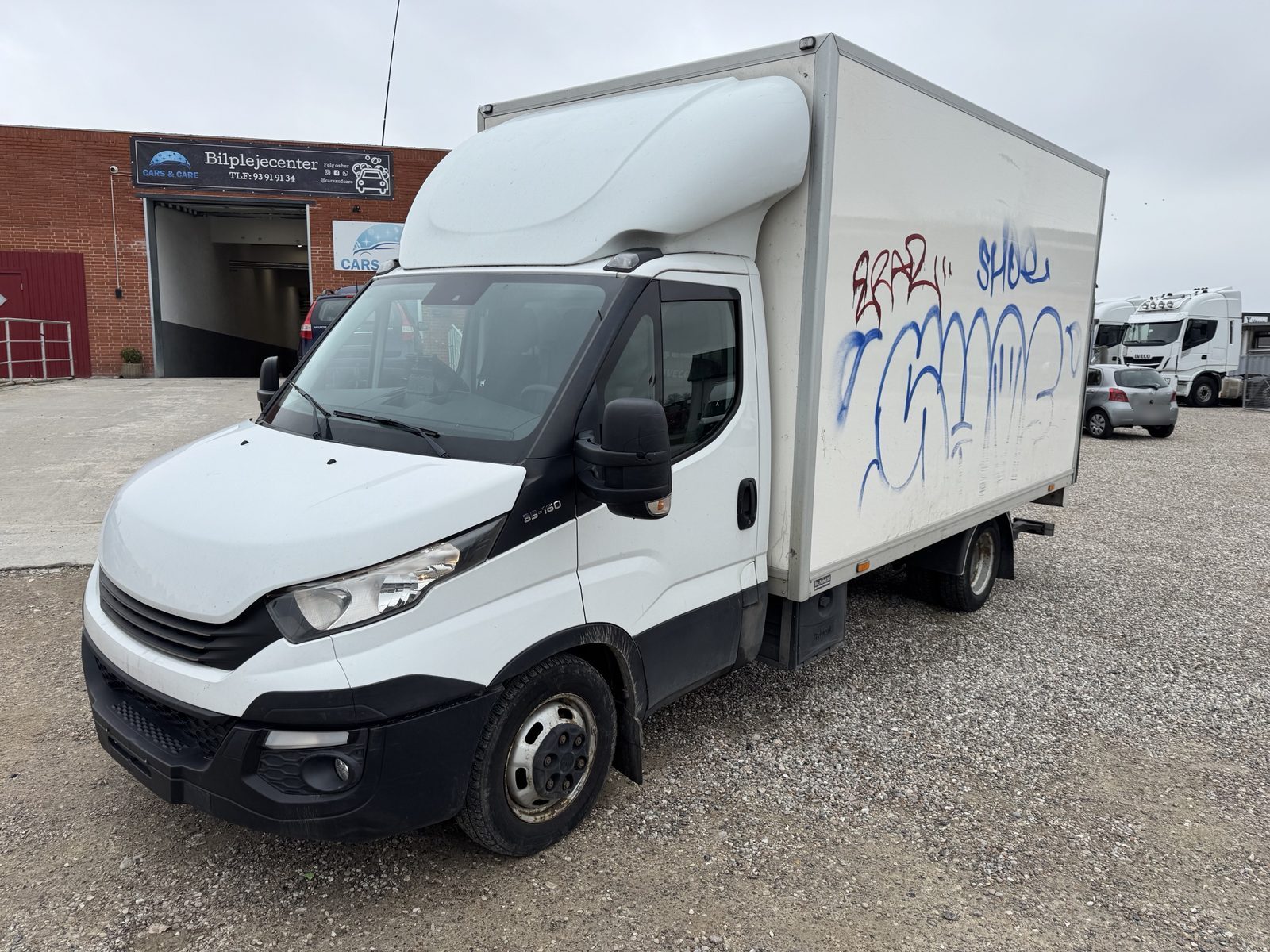 Hvid Iveco Daily ladvogn med blå og røde graffitibogstaver på siden af kassen foran værkstedet