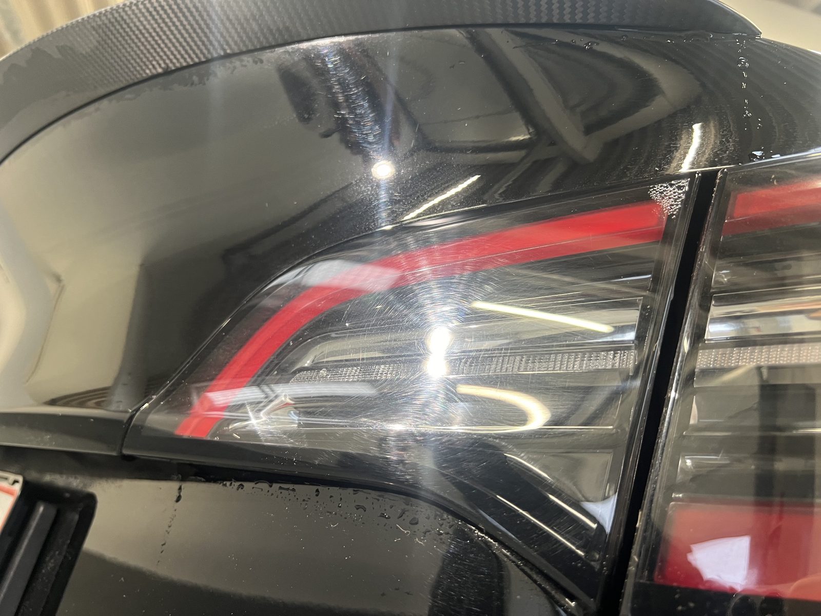 Baglygte på en sort Tesla fuld af fine ridser og swirls, der ses i lyset fra værkstedslamperne, før polering