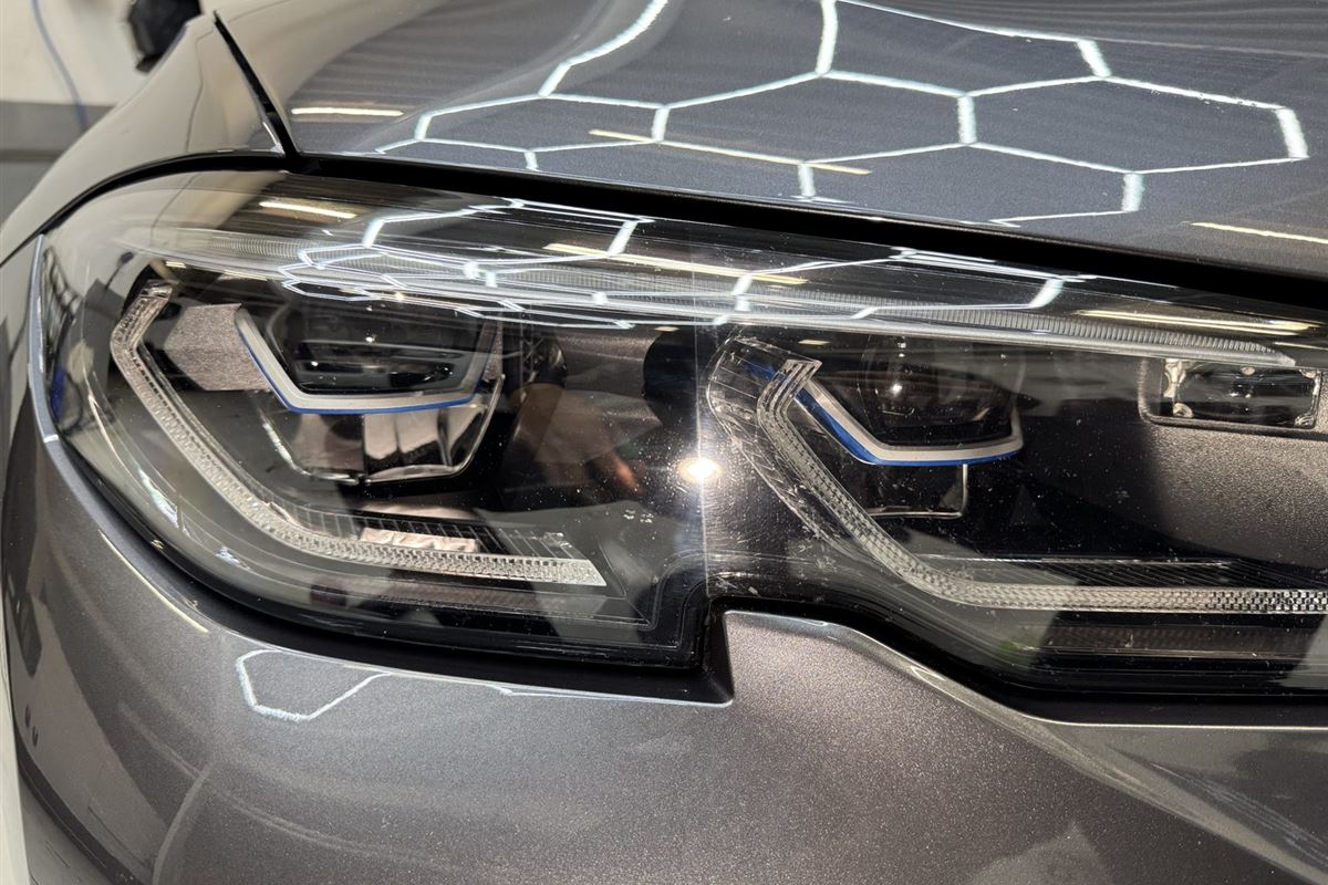 Poleret grå lak og forlygte på en BMW, hvor værkstedets sekskantede lys spejler sig i motorhjelmen