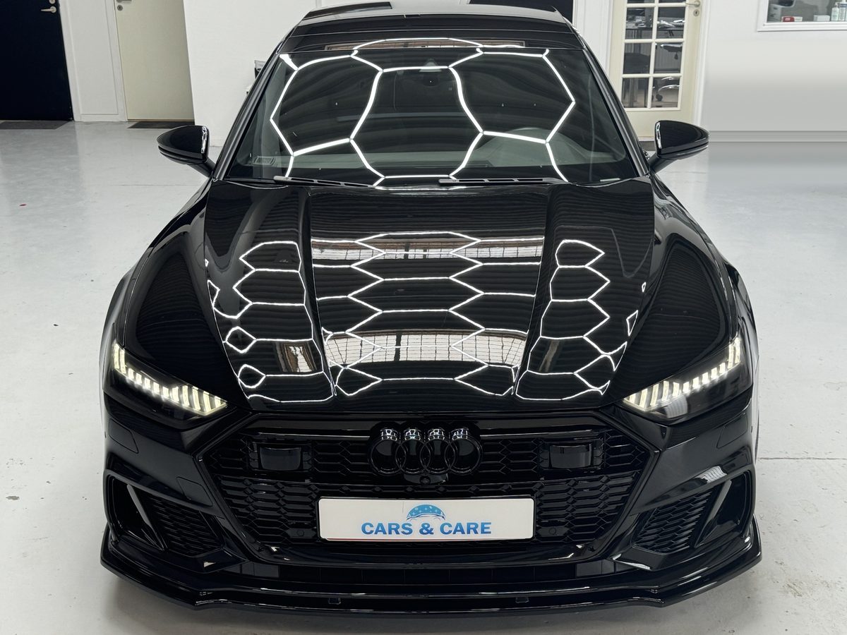 Sort Audi set forfra i værkstedet, med sekskantede lamper der spejler sig i den polerede motorhjelm