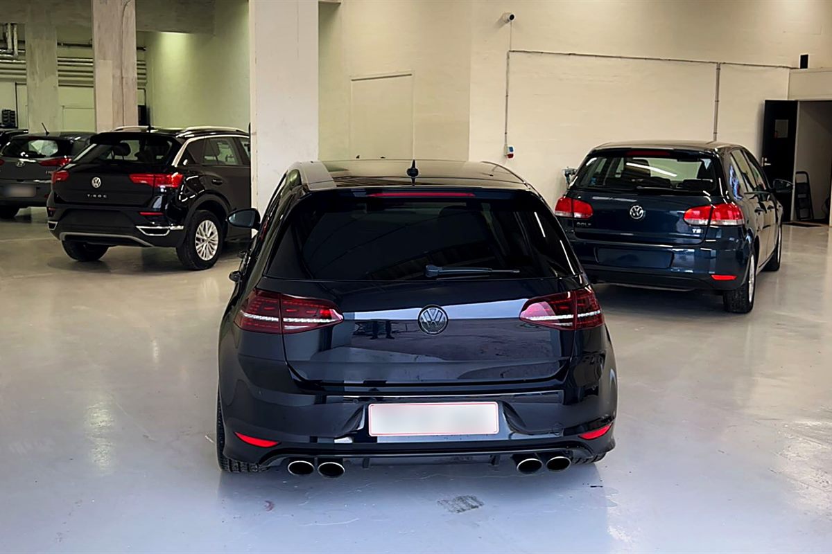 Værkstedet indefra med lyst gulv, hvide vægge og flere biler, nærmest en sort VW Golf set bagfra